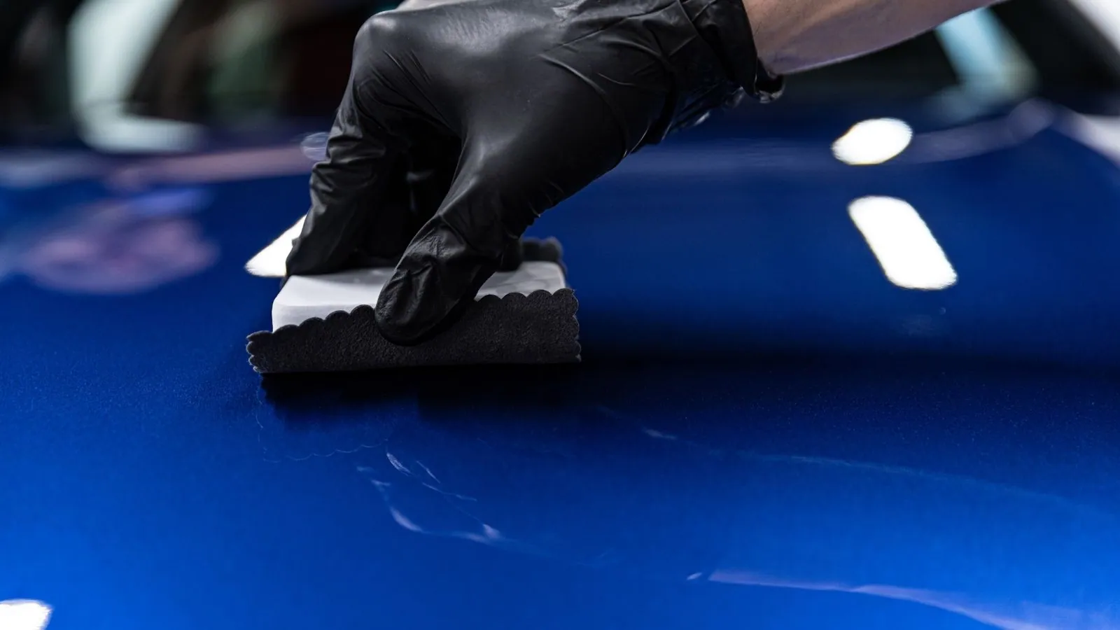 A detailer applying a ceramic coating to a car's paint with an applicator block