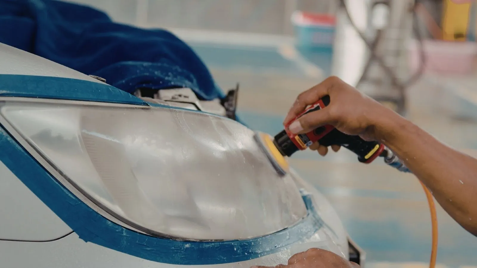 A detailer machine-polishing a taped-off headlight during restoration