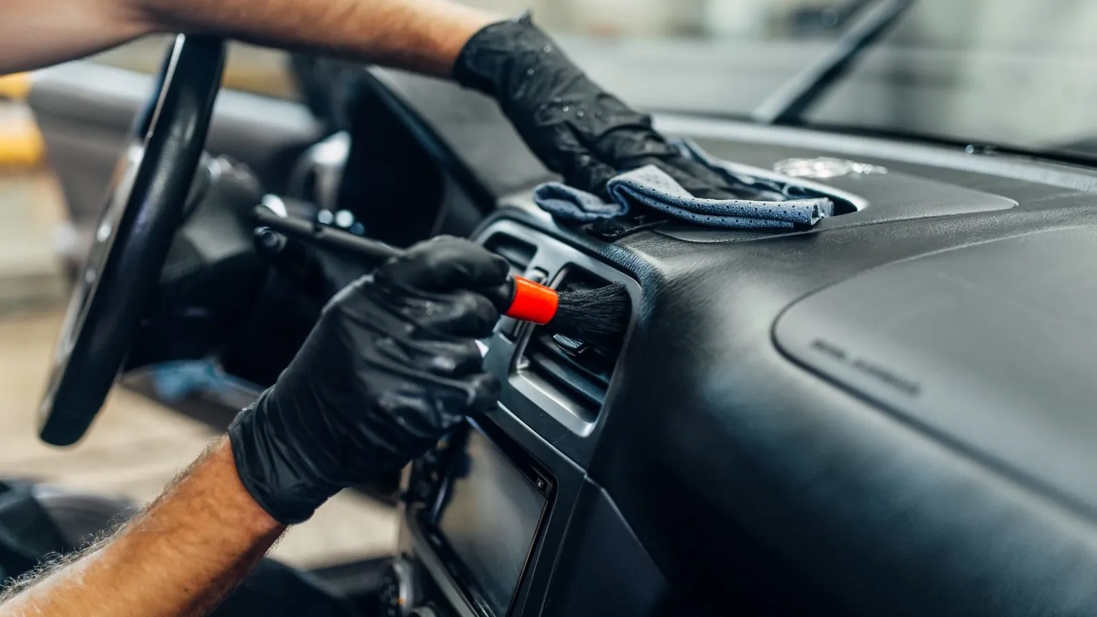 A detailer cleaning the dashboard vents with a detailing brush